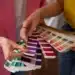 Dupla de mãos segurando diferentes amostras de cores, com foco nas paletas de tonalidades frias e quentes, para ajudar a escolher a cor ideal em casa.