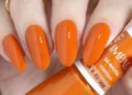 Unhas com esmalte laranja vibrante, tendência de cor para 2026.