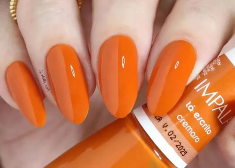 Unhas com esmalte laranja vibrante, tendência de cor para 2026.