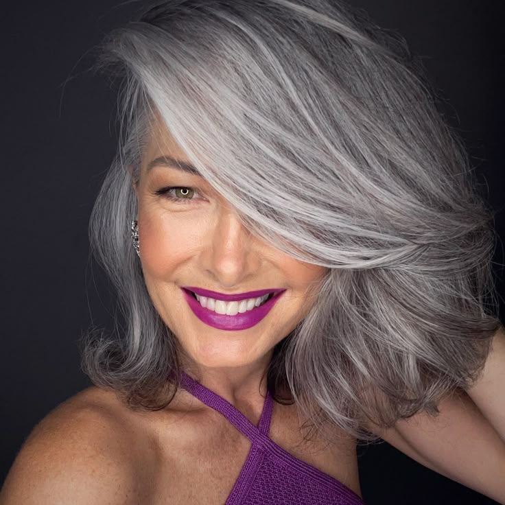 Mulher com cabelo grisalho e maquiagem roxa (batom) e roupa violeta, destacando como cores intensas como roxo e berinjela adicionam um ar contemporâneo e sofisticado ao visual.
