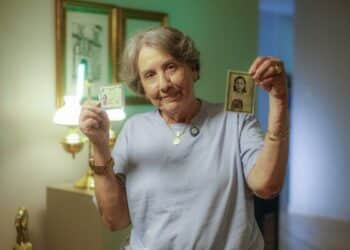 Idosa segurando a nova identidade e a antiga, representando a emissão gratuita para pessoas acima de 60 anos.