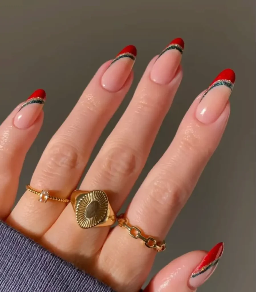 Unhas com francesinha natalina vermelha, decoradas com linhas douradas e de glitter.