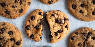 Vários cookies americanos frescos com gotas de chocolate, um deles partido ao meio, prontos para serem saboreados.