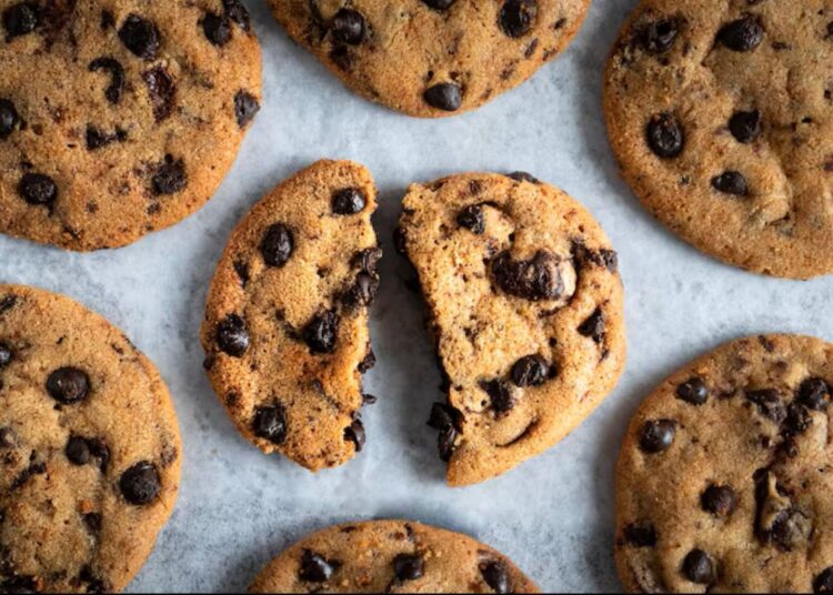 Vários cookies americanos frescos com gotas de chocolate, um deles partido ao meio, prontos para serem saboreados.