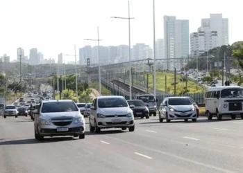 Imagem mostrando uma avenida movimentada com carros e edifícios ao fundo. A cena ilustra a discussão sobre o benefício de isenção do IPVA para idosos.