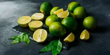 Limões frescos cortados ao meio, com casca verde e interior amarelo, sobre uma superfície escura.