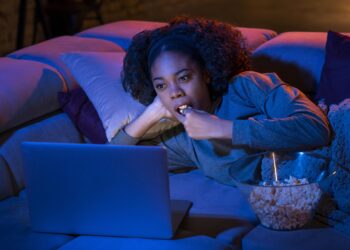 Mulher deitada no sofá com laptop e comendo pipoca à noite