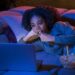 Mulher deitada no sofá com laptop e comendo pipoca à noite