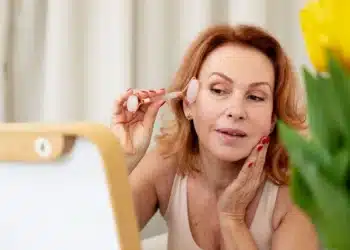Mulher utilizando um rolo de jade para cuidados faciais, realizando um procedimento de gua sha."