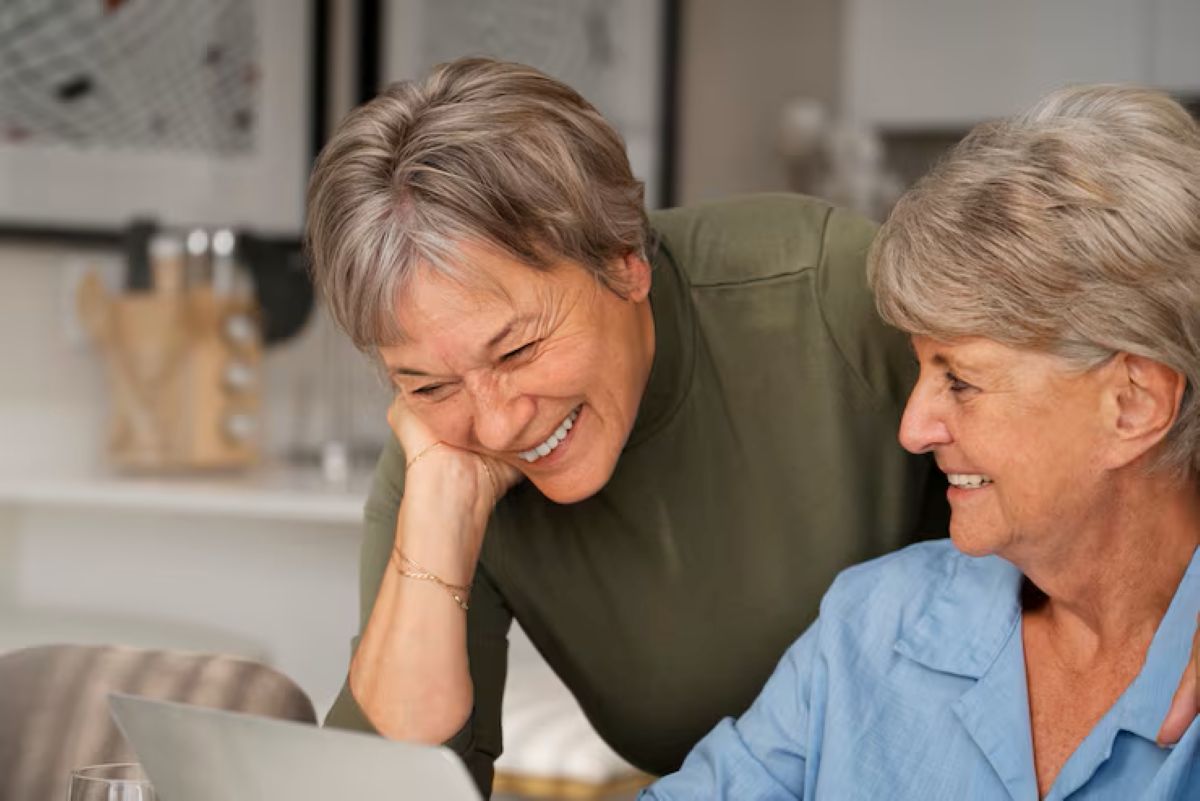 Mulheres sorrindo juntas enquanto visualizam algo no laptop, representando o empoderamento feminino na Previdência