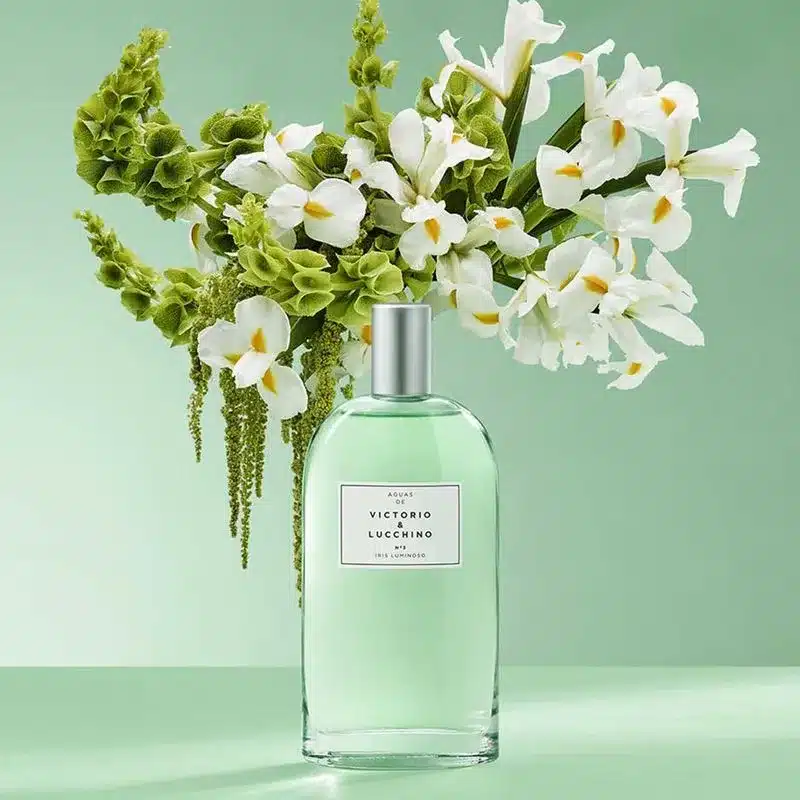 Iris Nº3 Victorio & Lucchino: O Perfume Elegante com Íris e Frescor Contemporâneo Frasco verde-claro do perfume Iris Nº3 LUMINOSO da Victorio & Lucchino em frente a um buquê de flores de íris brancas, representando o aroma intenso e refinado.