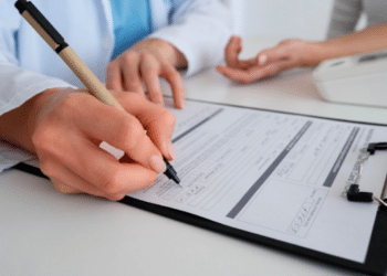 Profissional de saúde preenchendo formulário médico em prancheta durante consulta com paciente