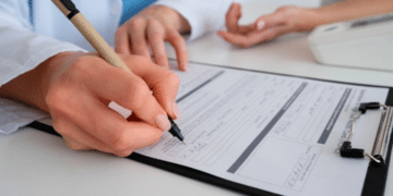 Profissional de saúde preenchendo formulário médico em prancheta durante consulta com paciente