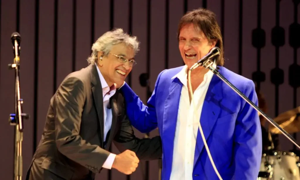 Caetano Veloso e Roberto Carlos Caetano Veloso e Roberto Carlos se cumprimentando e sorrindo durante uma apresentação ao vivo, refletindo sua amizade e respeito mútuo.