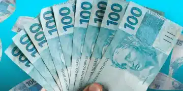 Mão segurando várias notas de 100 reais brasileiras com fundo azul claro