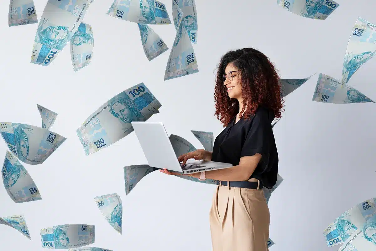 Mulher usando laptop e dinheiro caindo ao redor Mulher sorrindo usando laptop com notas de cem reais voando ao redor em fundo claro