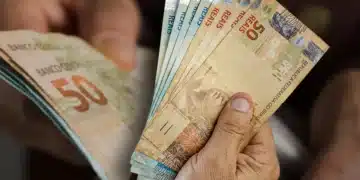Pessoa segurando várias notas de dinheiro em reais brasileiros, destacando cédulas de 50 e 2 reais.