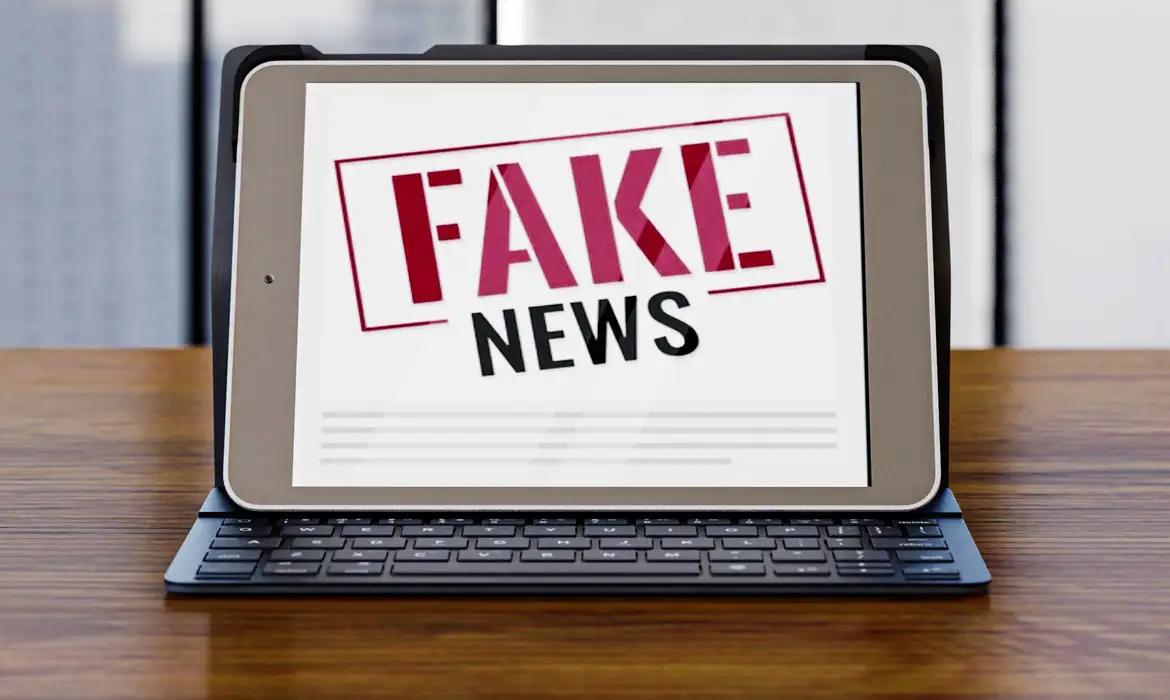 Combate eficaz às Fake News na era digital Tablet com a expressão FAKE NEWS exibida em vermelho e preto sobre mesa de madeira