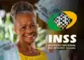 Idosa sorrindo enquanto segura cédulas de 100 reais com o logo do INSS ao fundo. Tema sobre os pagamentos do INSS.