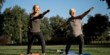 Senhor e senhora idosos praticando yoga no parque em tapetes de exercícios sob céu azul claro