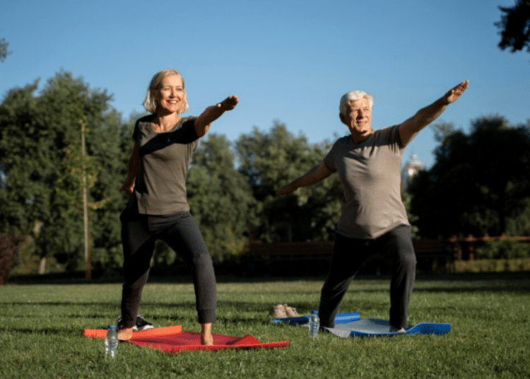 Senhor e senhora idosos praticando yoga no parque em tapetes de exercícios sob céu azul claro