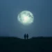 Casal observando uma lua gigante em meio à neblina ao anoitecer.