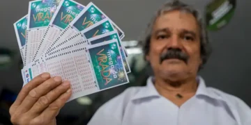 Homem segurando bilhetes da Mega da Virada, alertando sobre sites falsos que se passam pelas loterias da Caixa.
