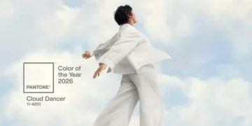 Pessoa vestindo roupas brancas posando diante de um céu suave, ilustrando a cor Pantone Cloud Dancer, eleita a cor de 2026.