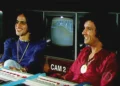 Caetano Veloso e Roberto Carlos sorrindo juntos durante uma gravação de TV, com uma tela de monitor ao fundo, simbolizando a amizade entre eles.