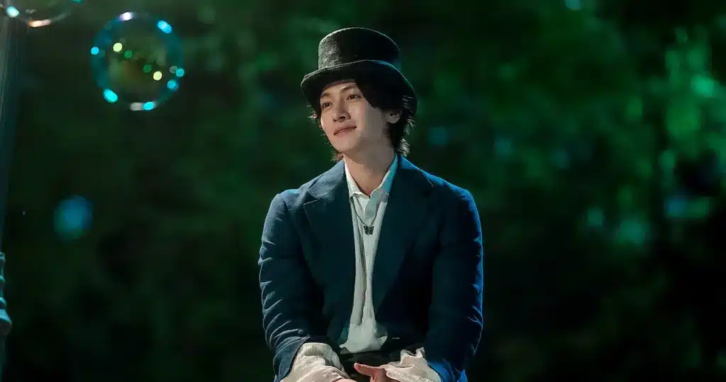 The Sound of Magic Homem misterioso sentado em um parque de diversões, com uma expressão tranquila e cercado por bolhas, em uma cena de The Sound of Magic.