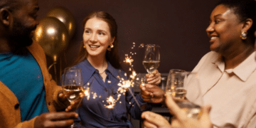 Grupo de amigos felizes brindando com taças de vinho branco e segurando fogos de artifício.