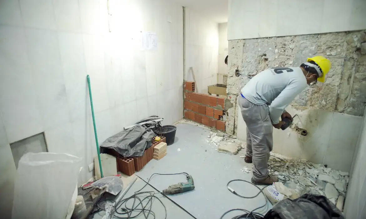 Reforma residencial com técnicas de demolição e construção Trabalhador com capacete amarelo realizando demolição em parede interna de reforma residencial