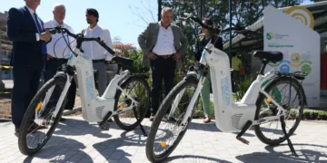 Bicicletas elétricas brancas movidas a hidrogênio expostas com pessoas observando ao fundo