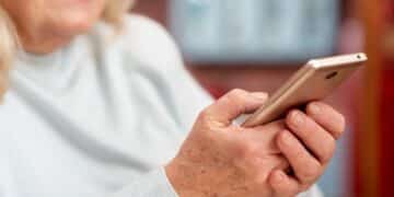 Close-up de uma pessoa mais velha sorrindo, digitando e enviando mensagens de bom domingo ou desejos de fim de semana pelo celular.