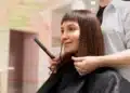 Mulher sorrindo enquanto faz o corte de cabelo no salão, com cabelo liso e franja.