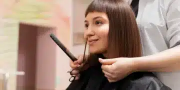 Mulher sorrindo enquanto faz o corte de cabelo no salão, com cabelo liso e franja.