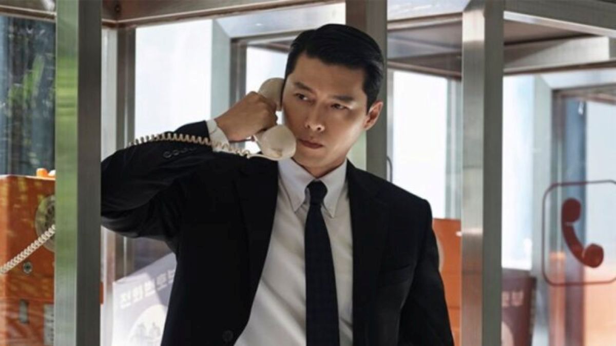 Cena de Made in Korea, com Hyun Bin em um telefonema tenso, caracterizado por seu traje formal e cenário dos anos 1970.