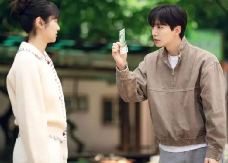 Cena de Cashero, com o protagonista mostrando uma nota de dinheiro para a personagem feminina, em um cenário ao ar livre.