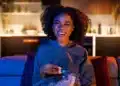 Mulher sorrindo enquanto assiste TV, segurando uma tigela de pipoca em ambiente aconchegante, com iluminação suave, simbolizando uma noite tranquila para maratonar doramas.