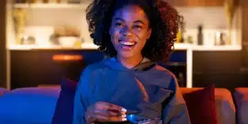 Mulher sorrindo enquanto assiste TV, segurando uma tigela de pipoca em ambiente aconchegante, com iluminação suave, simbolizando uma noite tranquila para maratonar doramas.