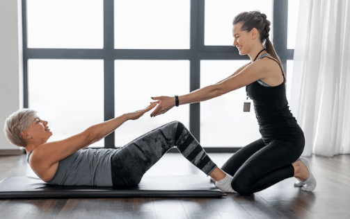 Idosa fazendo exercício abdominal auxiliada por personal trainer durante treino funcional em ambiente interno