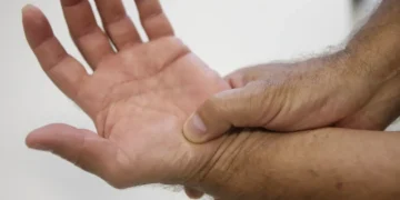 Pessoa segurando o pulso com a mão direita demonstrando dor ou desconforto no punho