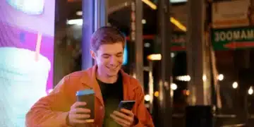 Jovem sorrindo à noite enquanto segura um café e lê mensagem no celular, representando frases de boa noite para WhatsApp.