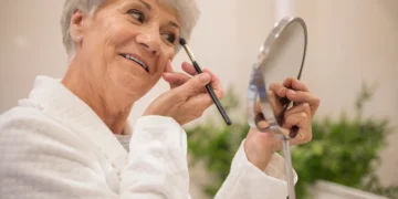 Mulher aplicando maquiagem com pincel, realçando sua beleza e rejuvenescendo a aparência.