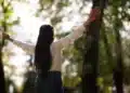 Mulher de braços abertos em meio à natureza simbolizando um novo começo cheio de esperança.