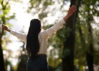 Mulher de braços abertos em meio à natureza simbolizando um novo começo cheio de esperança.