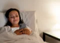 Mulher sorrindo na cama enquanto envia uma mensagem no celular, preparando-se para descansar após um dia cansativo de segunda-feira.