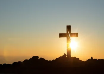 Imagem de uma cruz contra o pôr do sol, simbolizando fé e esperança para o domingo.