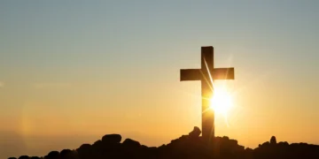 Imagem de uma cruz contra o pôr do sol, simbolizando fé e esperança para o domingo.