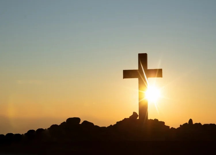 Imagem de uma cruz contra o pôr do sol, simbolizando fé e esperança para o domingo.